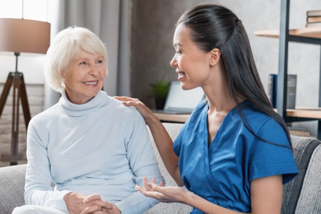 A nurse talking to an elderly woman on a couch.