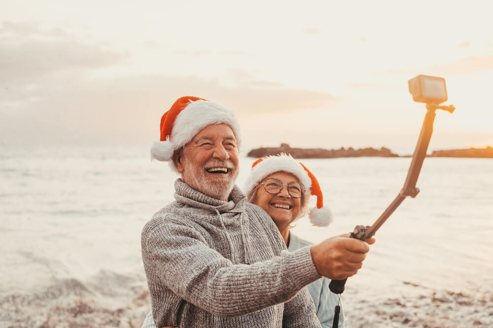 A senior couple in Santa hats taking a selfie on the beach.